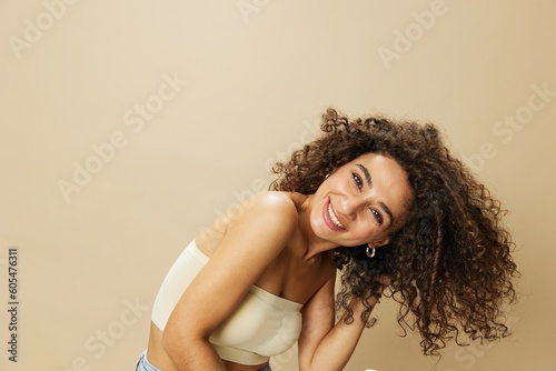 Woman dries curly afro hair with blow dryer, home beauty care styling products hair, smile on beige background
