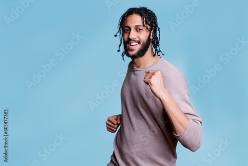 Happy handsome arab man dancing and partying while looking at camera with carefree facial expression. Young cheerful smiling person moving hands and enjoying music portrait