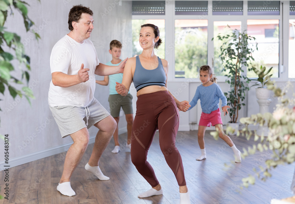 Smiling mother and father learning dynamic boogie-woogie in pair in dance studio during family class