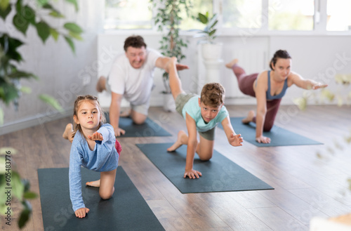 Family with two children doing yoga on mats in fitness studio..