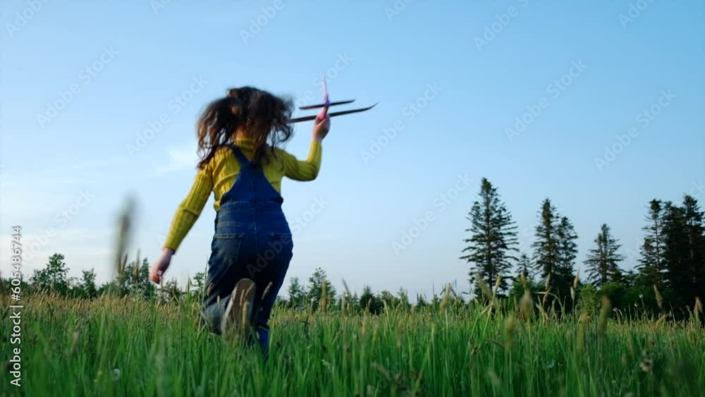 Silhouette of happy little girl child running with toy airplane on field in sunset light. Children play toy airplane on blue sky background. Preteen dreams of flying and becoming pilot. Slow motion