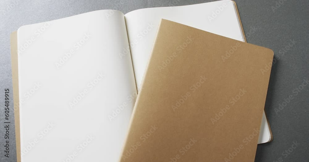 Close up of open blank book and brown notebook with copy space on gray background in slow motion