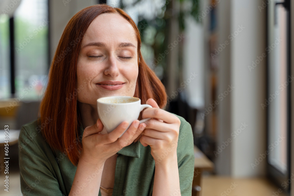 Beautiful redhead Irish young woman enjoying the smell of aroma coffee in modern office interior