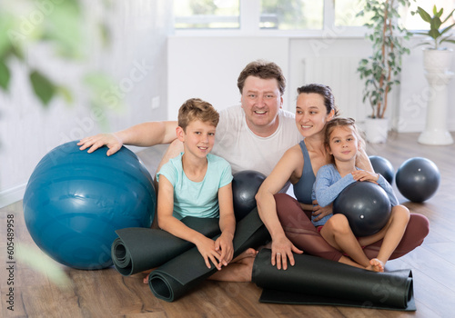 Portrait of happy family engaged in pilates sitting on the floor with black mats and softballs in hands in light room