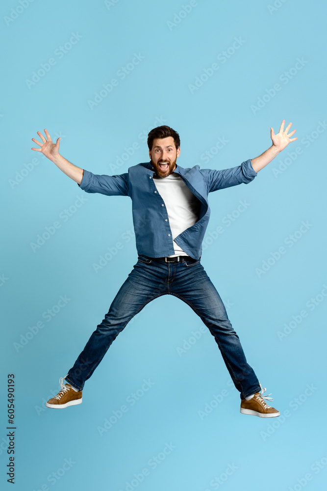 Full length portrait of a handsome emotional bearded man jumping high up on isolated blue background Full length portrait of a handsome emotional bearded man jumping high up on isolated blue background