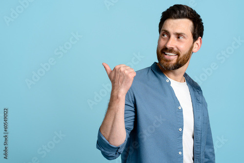 Studio portrait smiling handsome bearded pointing aside at copy ad space on isolated blue background
