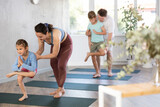 Careful parents helping their son and daughter to make chair pose of yoga in training room