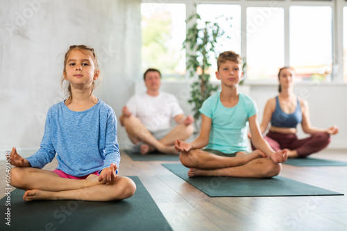 Positive pre-teen girl performing yoga exercises with brother and parents at gym, family health concept