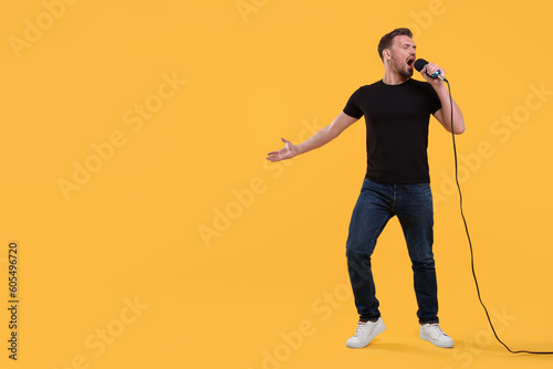Handsome man with microphone singing on yellow background. Space for text