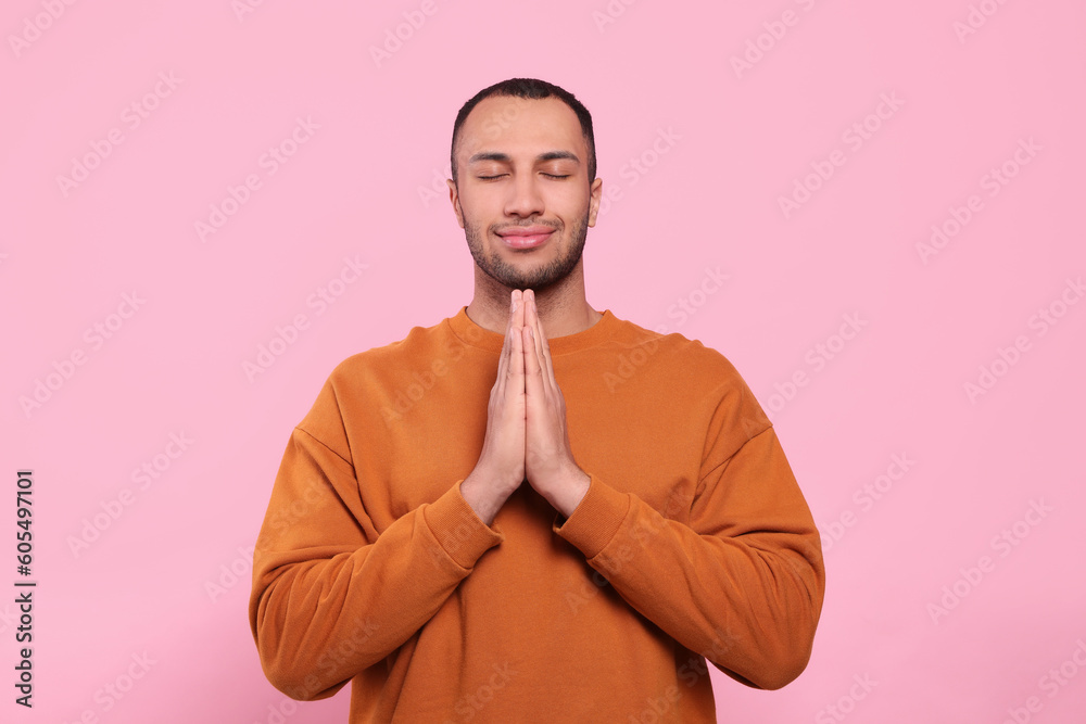 African American man with clasped hands praying to God on pink background