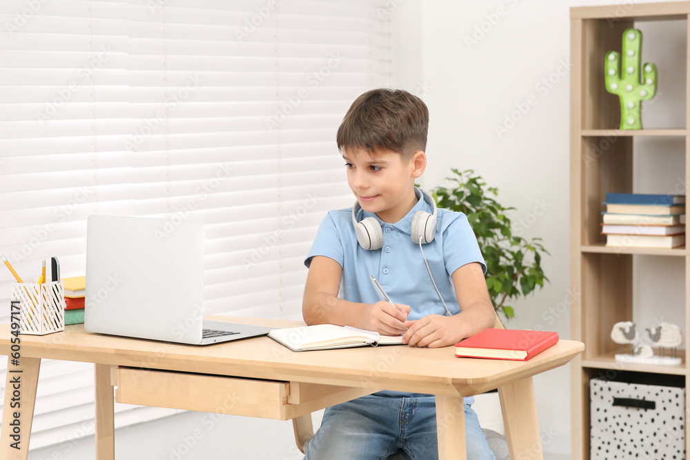 Boy writing in notepad near laptop at desk in room. Home workplace Boy writing in notepad near laptop at desk in room. Home workplace