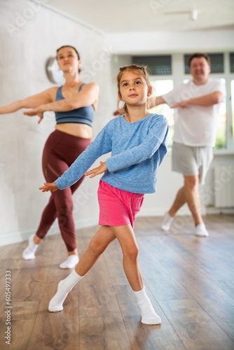 Pleasant little girl engaged in dance in group with her family in light room
