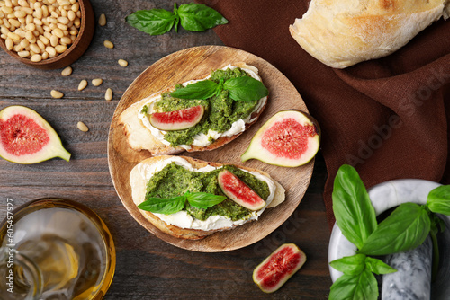Tasty bruschettas with cream cheese, pesto sauce, figs and fresh basil on wooden table, flat lay