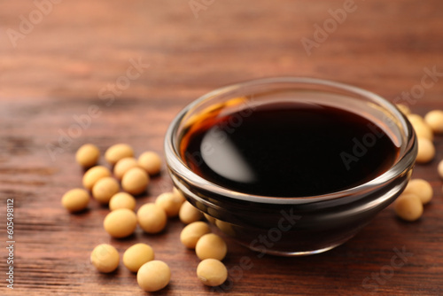 Soy sauce in bowl and soybeans on wooden table, closeup