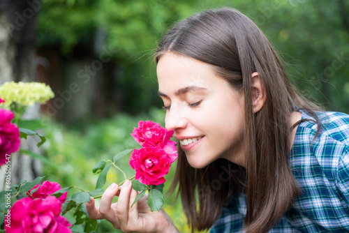 Beautiful girl smelling a rose flower in spring park. Young woman in flowering garden with roses. Beauty model with spring flowers. Happy spring. Pretty woman enjoying smell flowers in spring park.