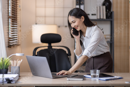 Happy caucasian young Asian woman using smart phone cellphone for calls, social media, mobile application online in office money financial planning Business And Education Concept.