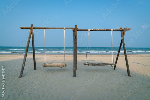 Swing made of wood and timber with two seats on the beach. Sea with horizon background. Travel or vacation concept.