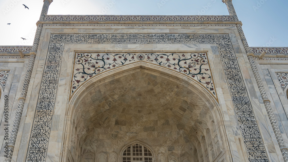 Details of the architecture of the beautiful Taj Mahal. The arched entrance, ornaments, inlays of precious stones on the white marble walls are visible. Blue sky. India. Agra.