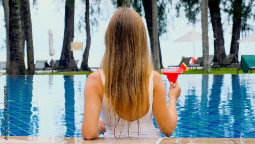 Woman relaxing in luxury beach resort pool, drinking non-alcoholic cocktail, enjoying nature and sunbathing. Suitable for luxury vacation and summer holiday. Back view © TravelMedia