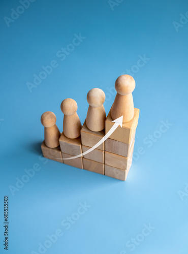 Leadership with business success concept. Rising up arrow and wooden figures standing on a growth graph chart steps arranged by wood cube blocks isolated on blue background, vertical style, top view.