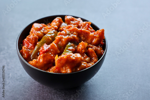 Schezwan Chicken or Dragon Chicken in black bowl at dark slate background. Szechuan Chicken is popular indo-chinese spicy dish with chilli peppers chicken and vegetables.
