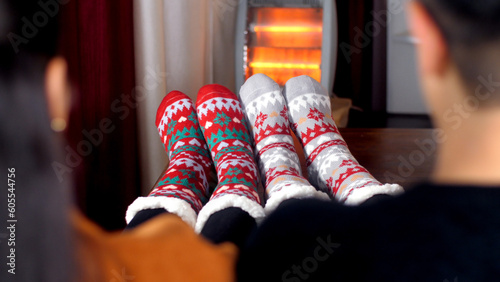 Two pairs of feet together wearing colorful woolen socks in front of a heater. A young Indian married couple enjoying the winters together at home - cold climate chilly weather love and romance