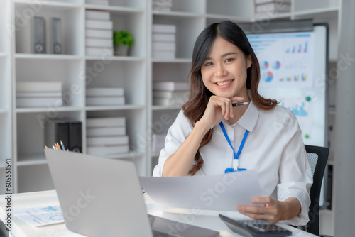Beautiful young female manager or company worker holding accounting documents, checking financial data or marketing reports working in office with laptop. Accountant consults on some document.
