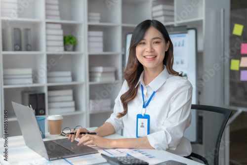 Happy smiling Asian businesswoman using laptop computer in the office. Beautiful young Asian female shopping or chatting online in social networks, freelance working on laptop projects.