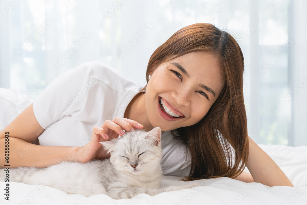 Young Asian woman lying on bed and playing small Scottish kitten on the room. Young Asian woman lying on bed and playing small Scottish kitten on the room.