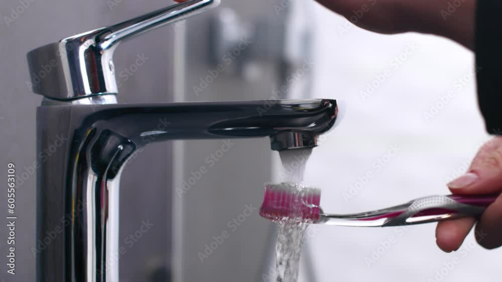 Person pours water on toothbrush in domestic bathroom, close up Person pours water on toothbrush in domestic bathroom, close up