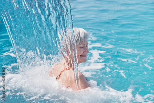 Senior caucasian smiling woman with gray hair enjoying falling on her shoulders flow of water.