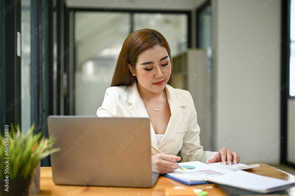 Focused Asian businesswoman reading and examining business reports at her desk Focused Asian businesswoman reading and examining business reports at her desk