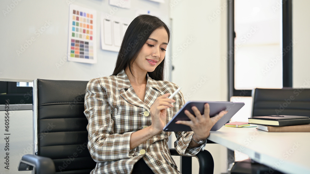 Charming Asian female web designer working on her work and using her digital tablet Charming Asian female web designer working on her work and using her digital tablet