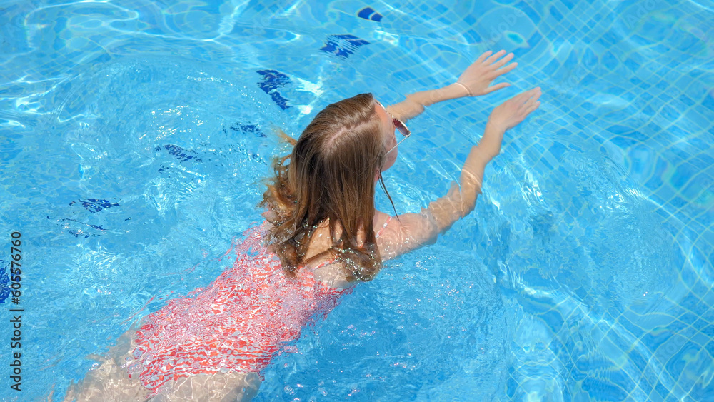 Woman in sunglasses swimming in pool in bikini and enjoing it