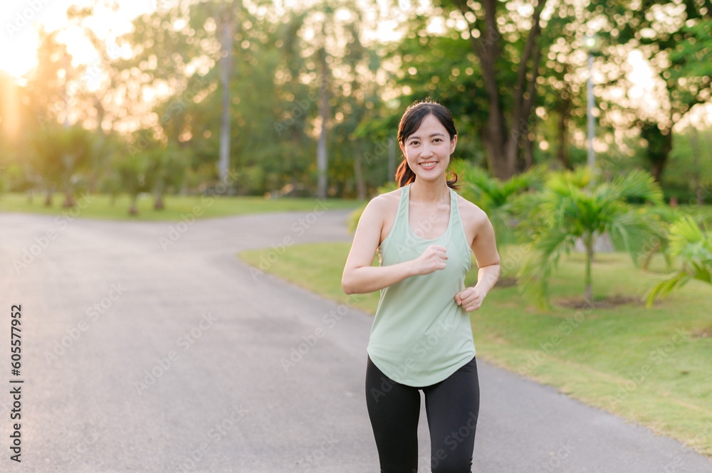 Fit Asian young woman jogging in park smiling happy running and enjoying a healthy outdoor lifestyle. Female jogger. Fitness runner girl in public park. healthy lifestyle and wellness being concept Fit Asian young woman jogging in park smiling happy running and enjoying a healthy outdoor lifestyle. Female jogger. Fitness runner girl in public park. healthy lifestyle and wellness being concept