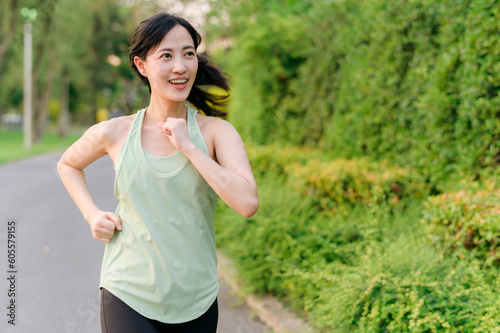 Fit Asian young woman jogging in park smiling happy running and enjoying a healthy outdoor lifestyle. Female jogger. Fitness runner girl in public park. healthy lifestyle and wellness being concept