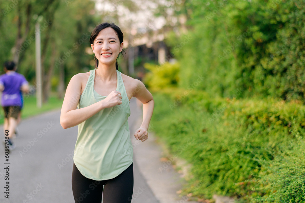 Fit Asian young woman jogging in park smiling happy running and enjoying a healthy outdoor lifestyle. Female jogger. Fitness runner girl in public park. healthy lifestyle and wellness being concept Fit Asian young woman jogging in park smiling happy running and enjoying a healthy outdoor lifestyle. Female jogger. Fitness runner girl in public park. healthy lifestyle and wellness being concept