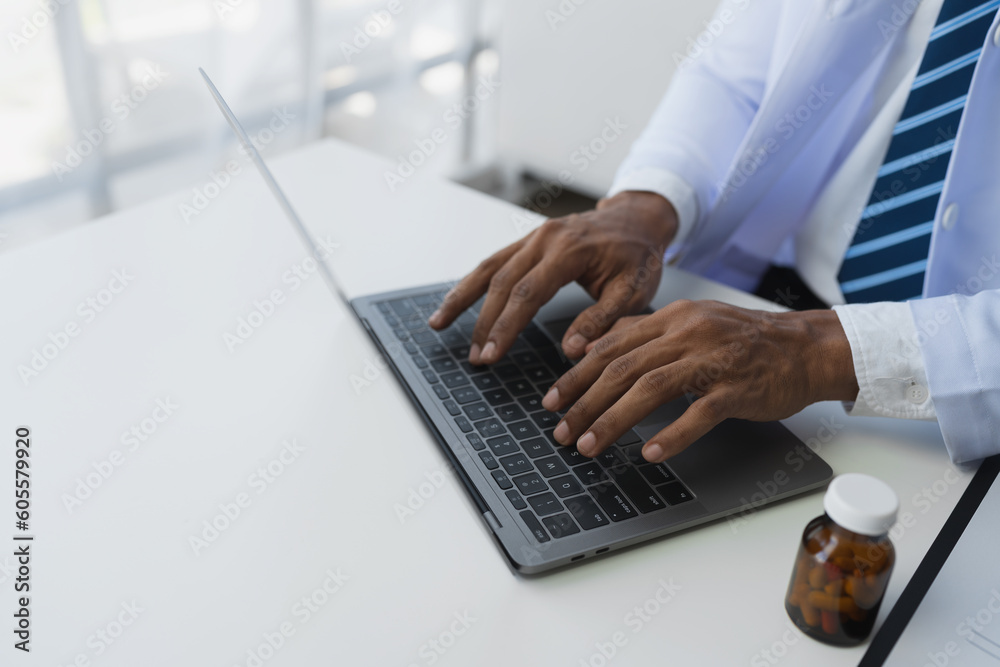 Doctor or researcher typing and looking at pill information on laptop while sitting at desk with pill bottle to analyze data and take notes on prescription. Medical and health insurance concept. Doctor or researcher typing and looking at pill information on laptop while sitting at desk with pill bottle to analyze data and take notes on prescription. Medical and health insurance concept.