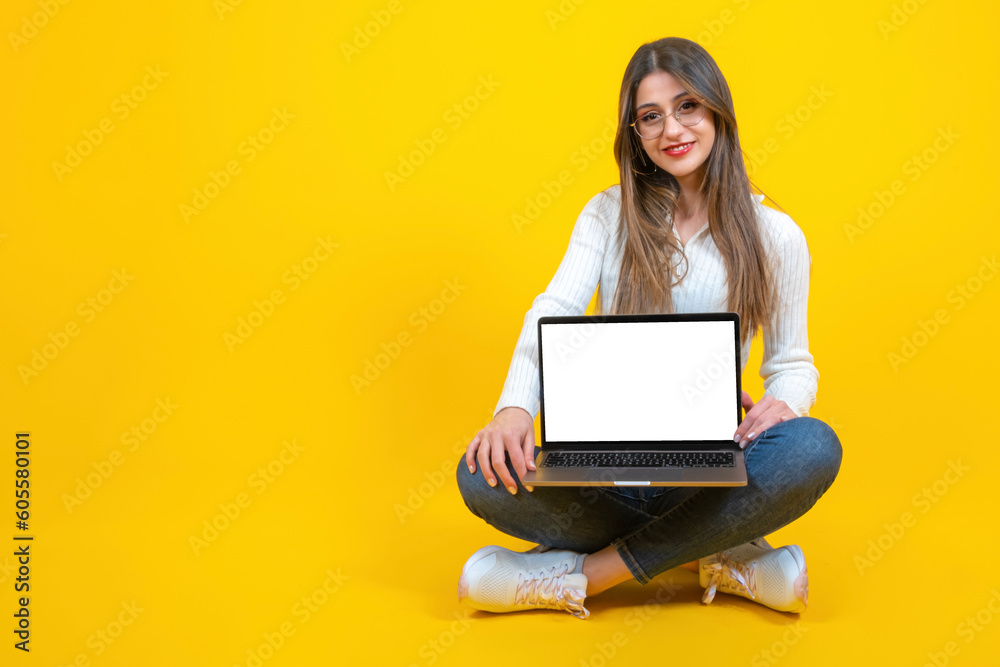 Naklejka premium Modern laptop mockup, real caucasian woman sitting ground holding modern laptop mockup. Smiling positive girl showing notebook with empty blank white screen. Yellow background, copy space. 