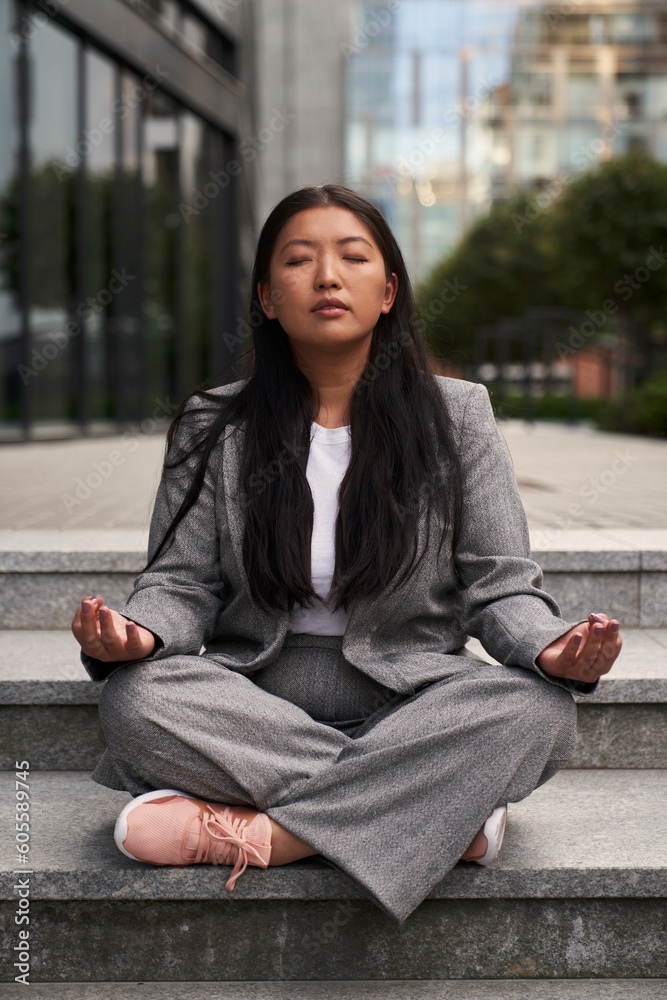Chinese woman in business outfit meditating out of the building. - obrazy, fototapety, plakaty 
