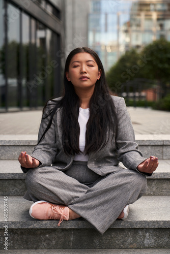 Chinese woman in business outfit meditating out of the building.