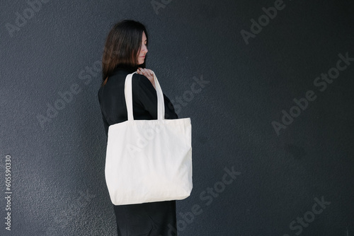 Woman holding white textile eco bag against urban city background. Ecology or environment protection concept. White eco bag for mock up.