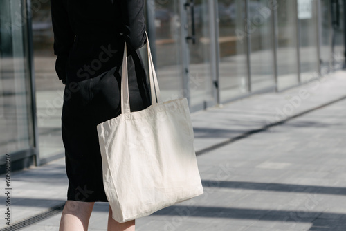 Woman holding white textile eco bag against urban city background. Ecology or environment protection concept. White eco bag for mock up.