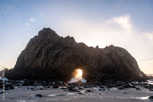 Wide-angle shot of the keyhole arch at Pfeiffer beach, California, whit the setting sun peeping through the central hole. Sunset on a winter evening in California.