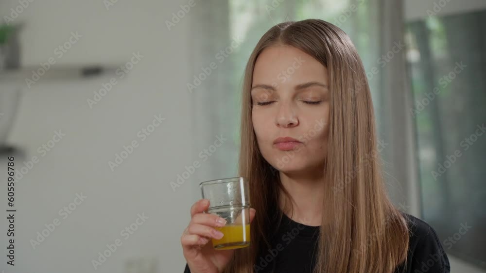 A beautiful caucasian girl in a black t-shirt drinks freshly squeezed orange juice with vitamin C. A fair-haired woman enjoys a fruit drink in a glass glass. European woman smiling at the camera. A beautiful caucasian girl in a black t-shirt drinks freshly squeezed orange juice with vitamin C. A fair-haired woman enjoys a fruit drink in a glass glass. European woman smiling at the camera.