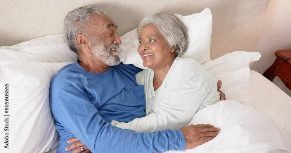 Happy senior biracial couple lying on bed, embracing and smiling, unaltered, in slow motion Happy senior biracial couple lying on bed, embracing and smiling, unaltered, in slow motion