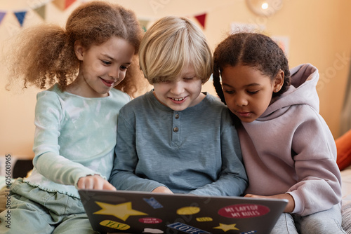 Group of three little children using laptop together at home and smiling photo