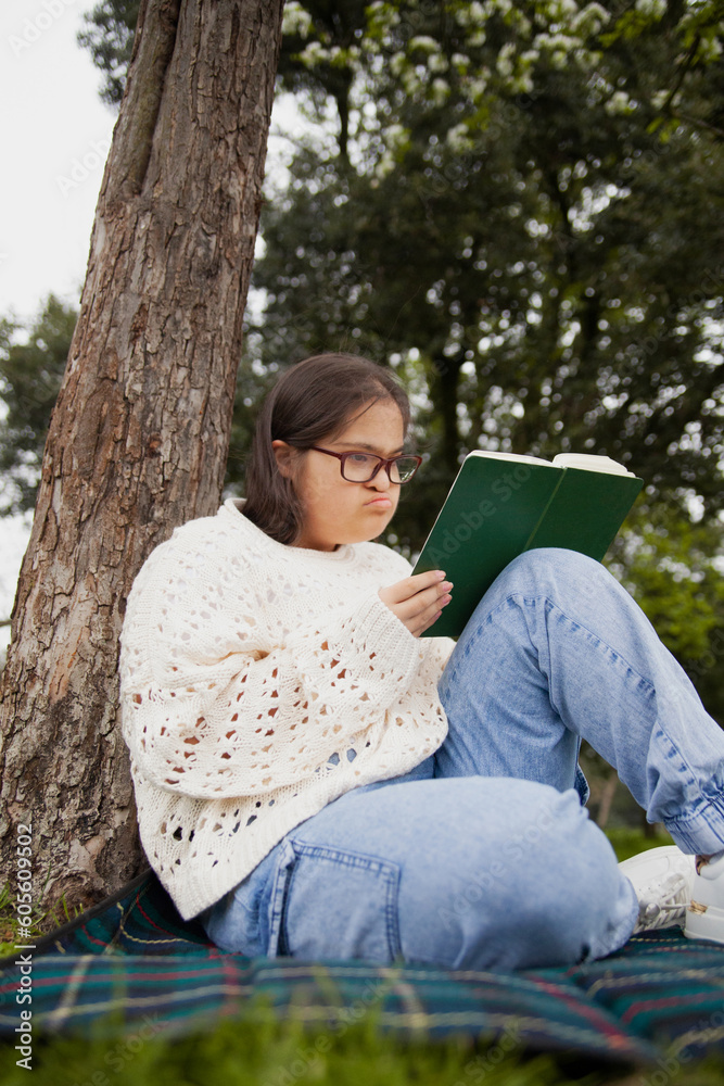 Fototapeta premium Curvy woman with Down syndrome reading in the park