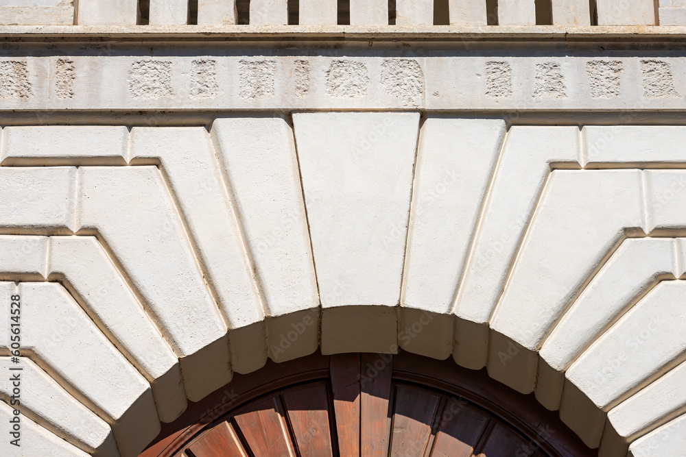 Fototapeta premium Closeup of a medieval white marble arch with keystone and brown wooden door, full frame, photography. Brescia downtown, Lombardy, Italy, Europe.