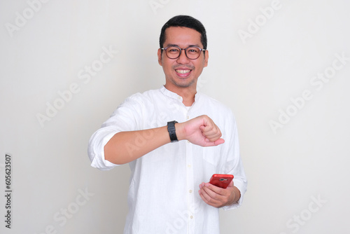 Adult Asian man smiling while holding mobile phone and showing his watch photo